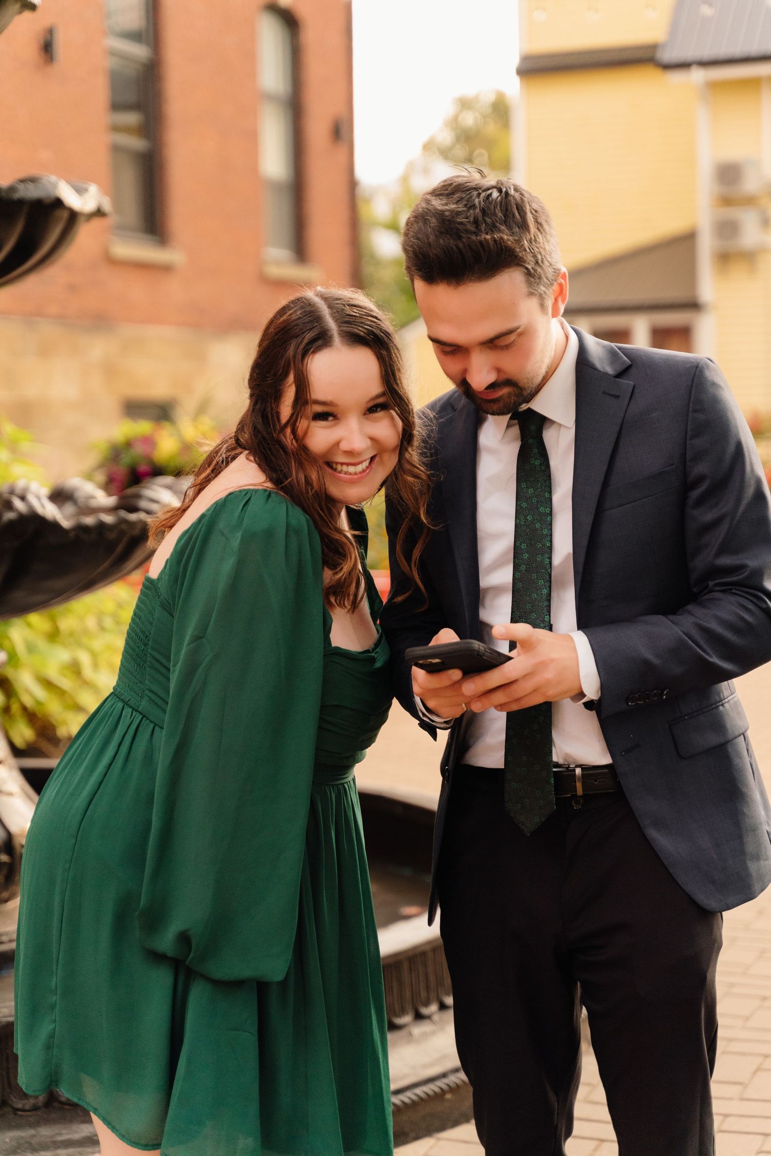 A couple in business attire share a joyful moment looking at a phone outdoors.