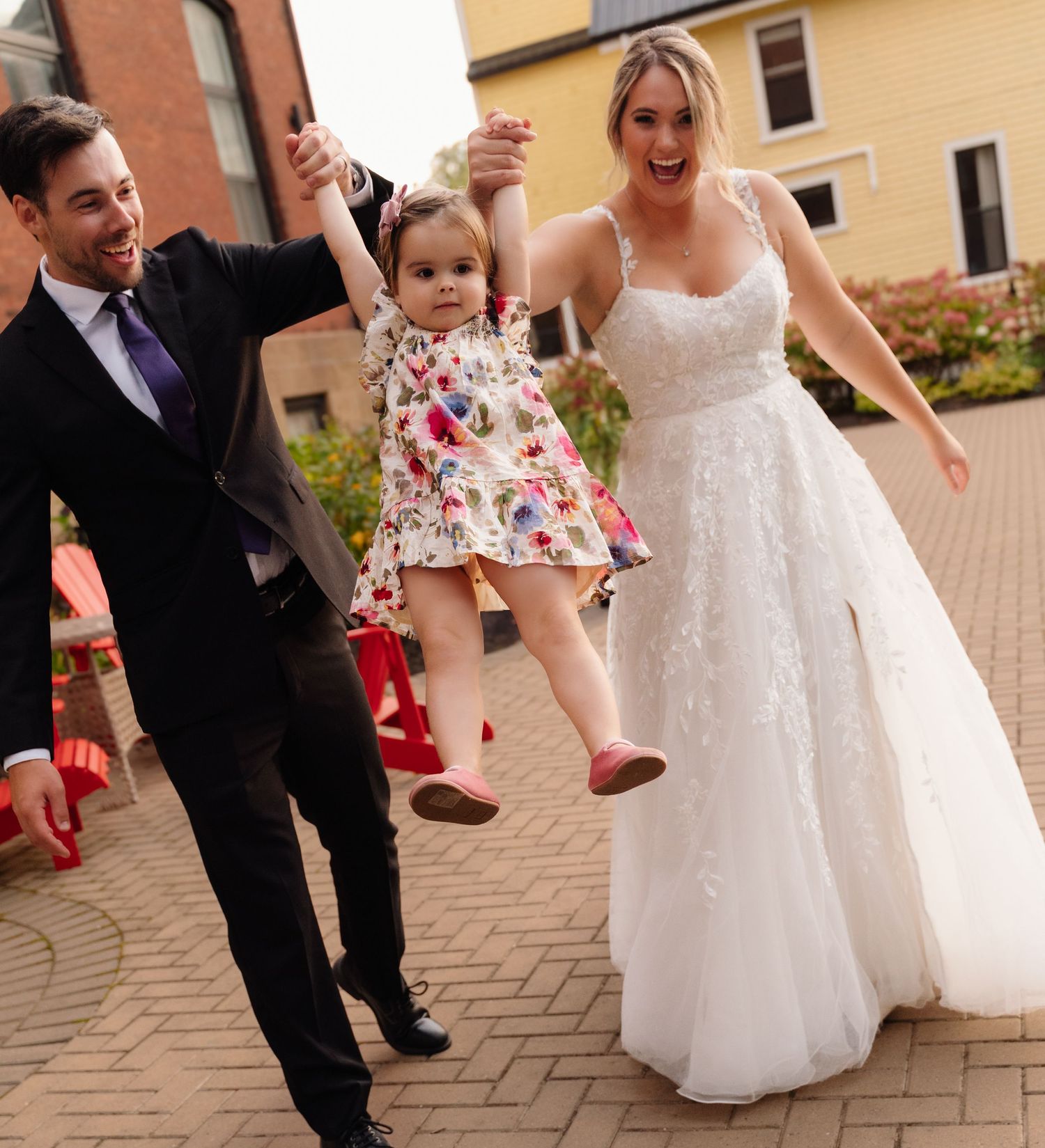 A joyful family moment as they swing a small child in floral dress between them.