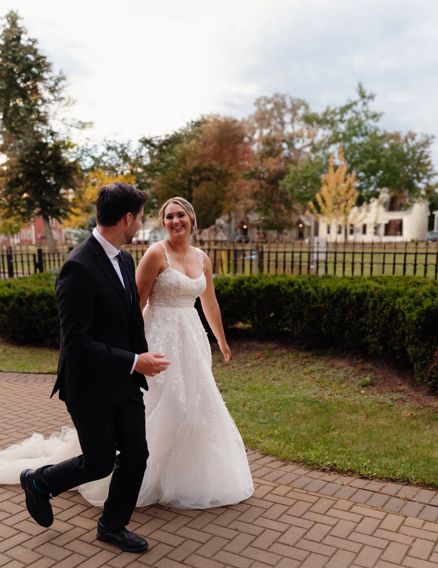Wedding couple shares a playful moment on a brick pathway surrounded by fall foliage.