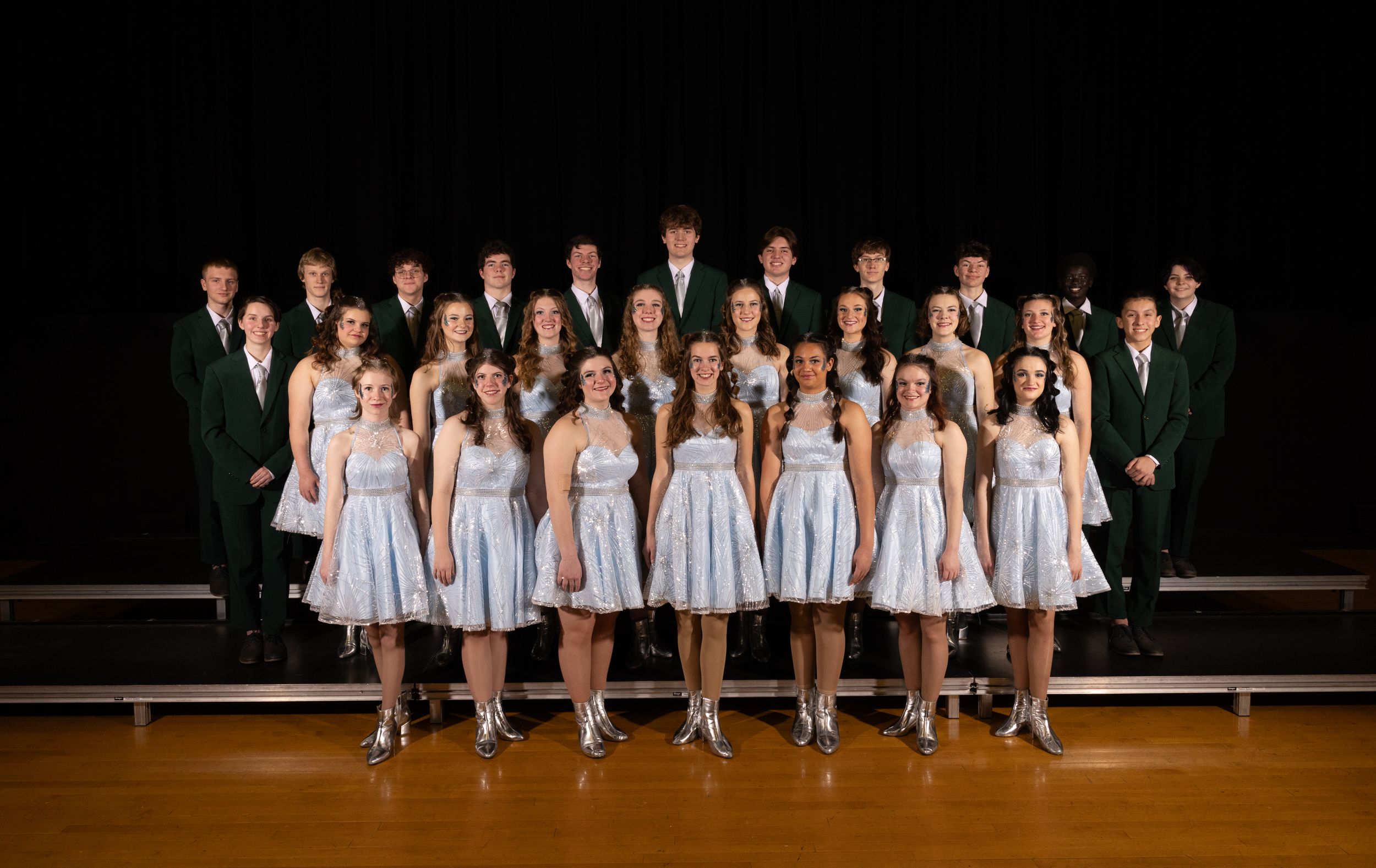 Dance group in light blue dresses performs on stage in synchronized formation.