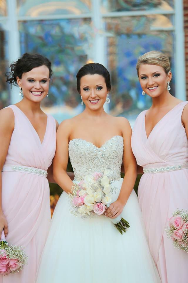 Bride in white gown poses with bridesmaids wearing pink dresses and holding bouquets.