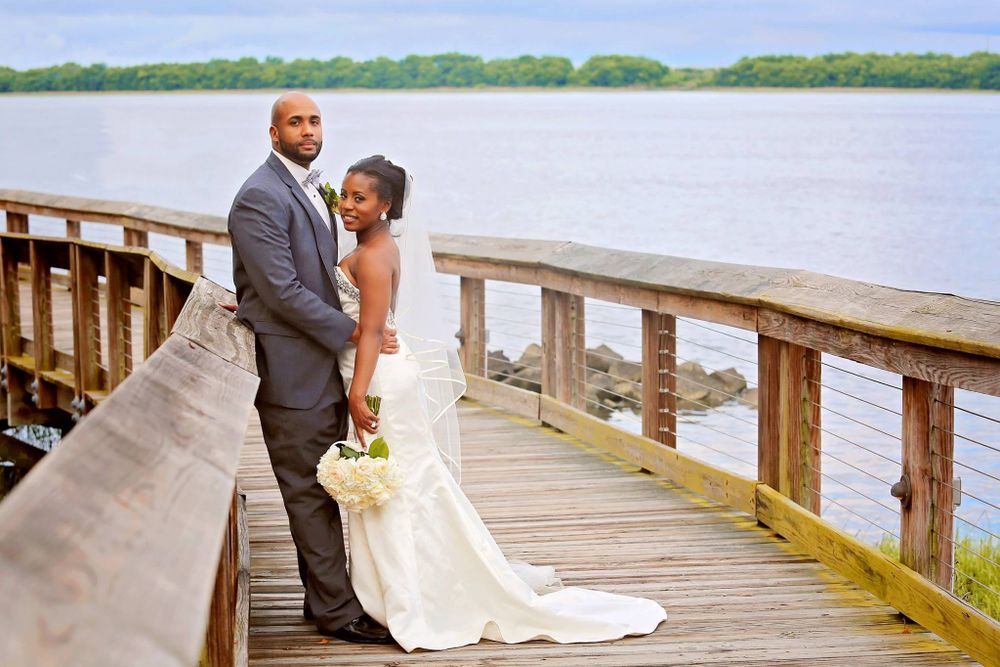 Newlyweds pose together on a wooden dock overlooking a serene lake.