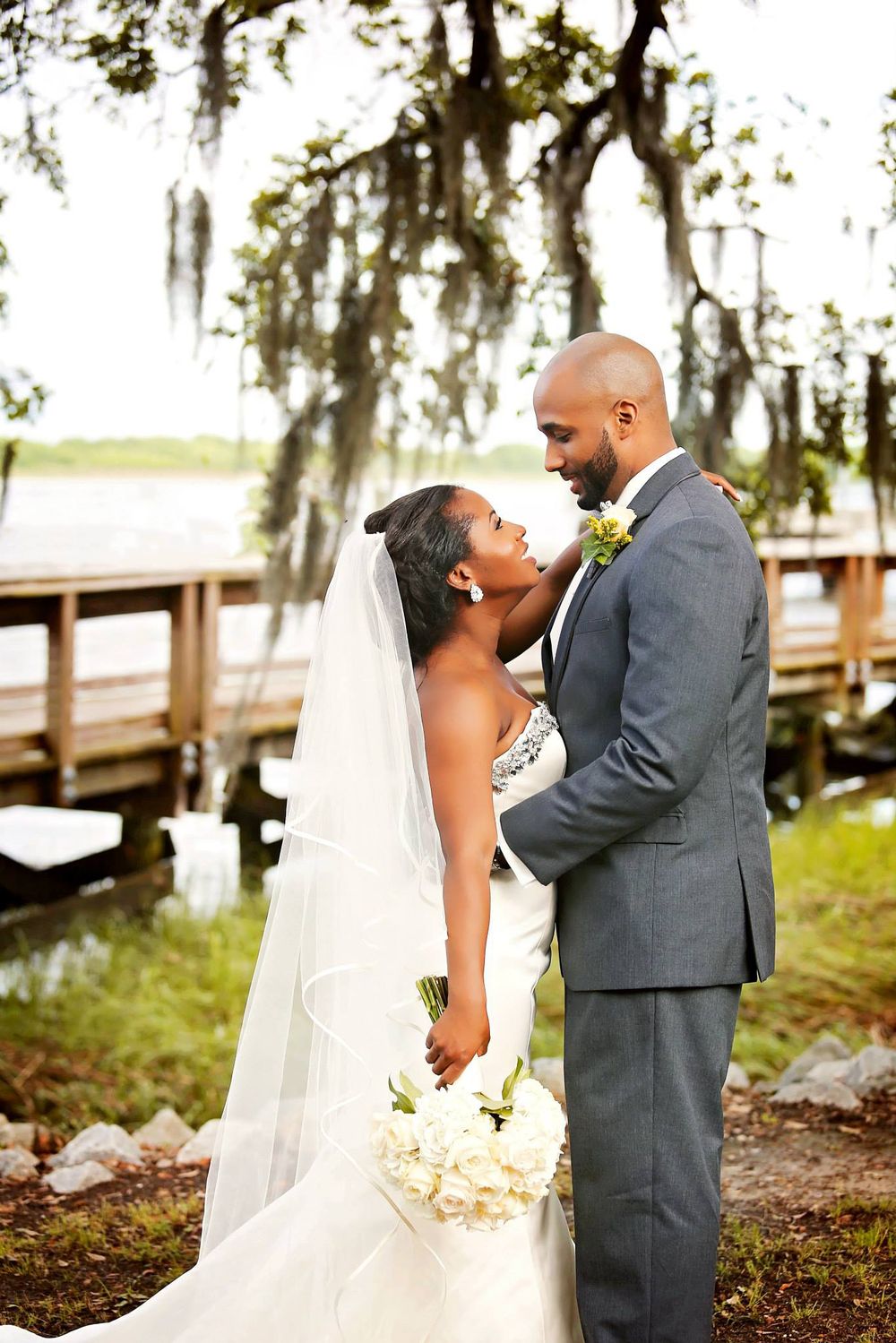 Wedding couple shares intimate moment on dock with Spanish moss hanging from trees.