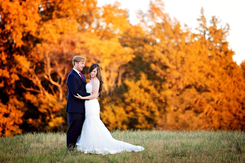 Romantic wedding couple embraces in front of vibrant orange autumn foliage at sunset.