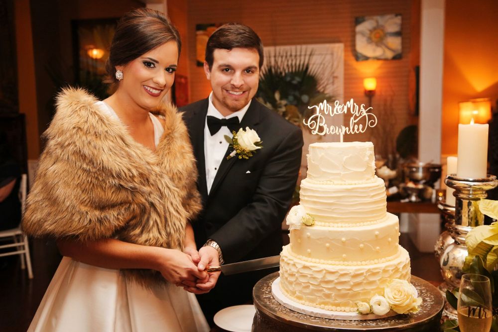A couple cuts their elegant white tiered wedding cake decorated with delicate details at their reception.