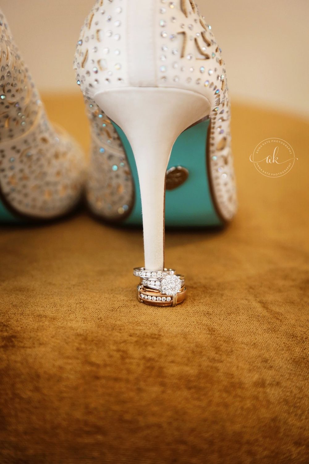 Wedding rings displayed creatively on white crystal-studded high heel shoe with blue sole.