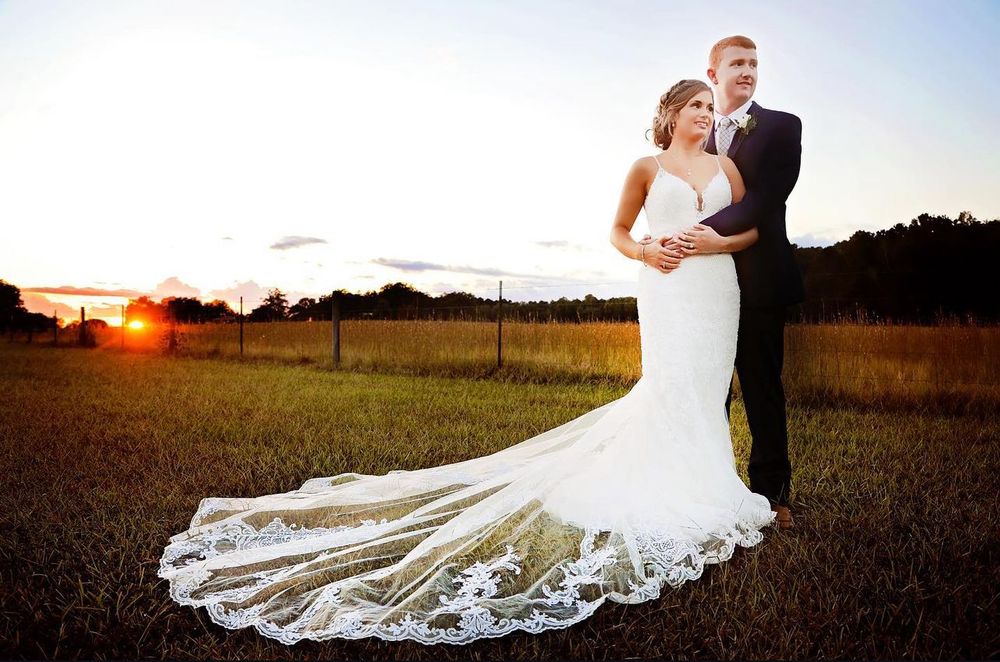 Sunset wedding portrait with bride in lace train dress in golden field.