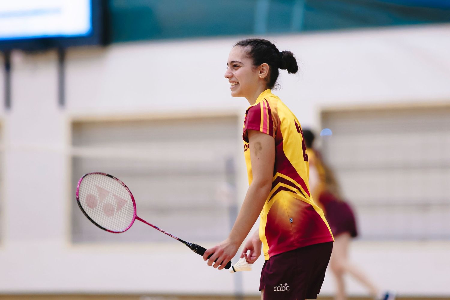 Athlete in yellow and red uniform playing badminton indoors.