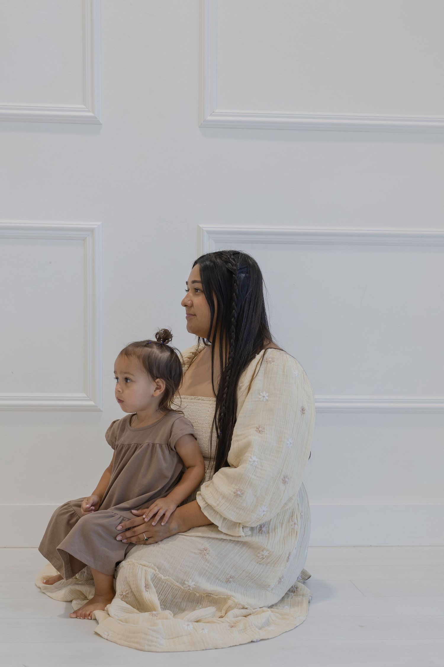 An intimate portrait of parent and child sitting together against a white paneled wall.