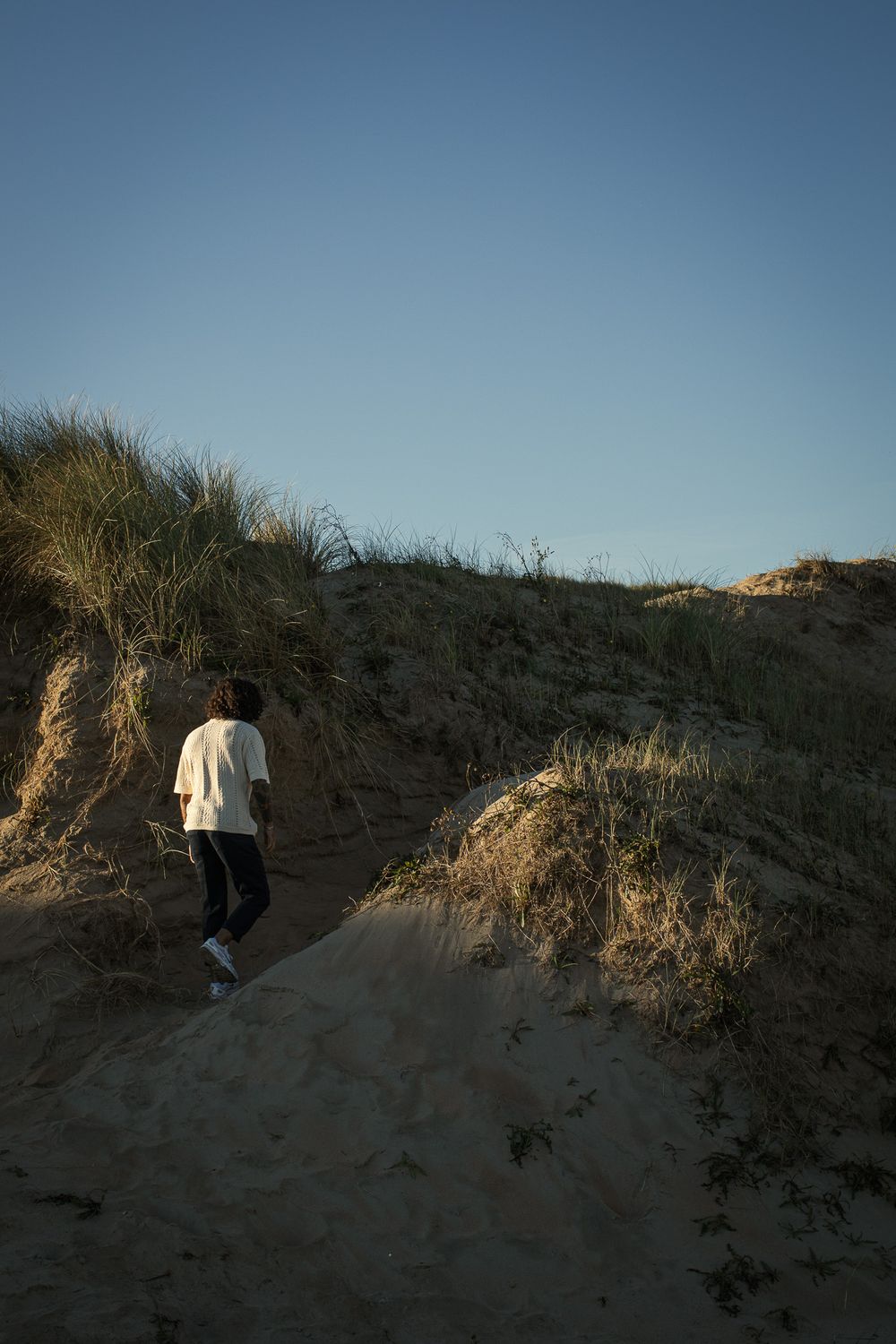 Figure in white clothing walking along sandy dunes at dusk.