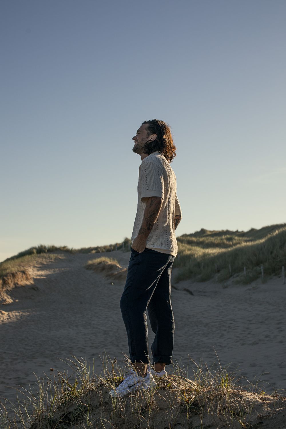 Person standing on coastal sand dunes against clear blue sky.
