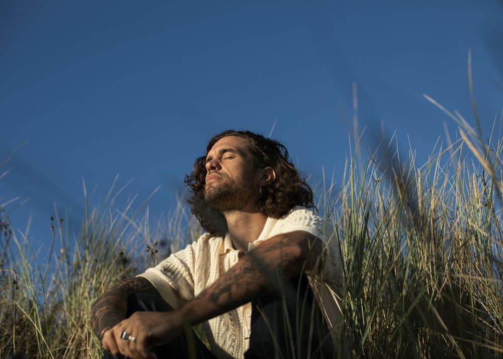 Person lying in tall grass under bright blue sky.