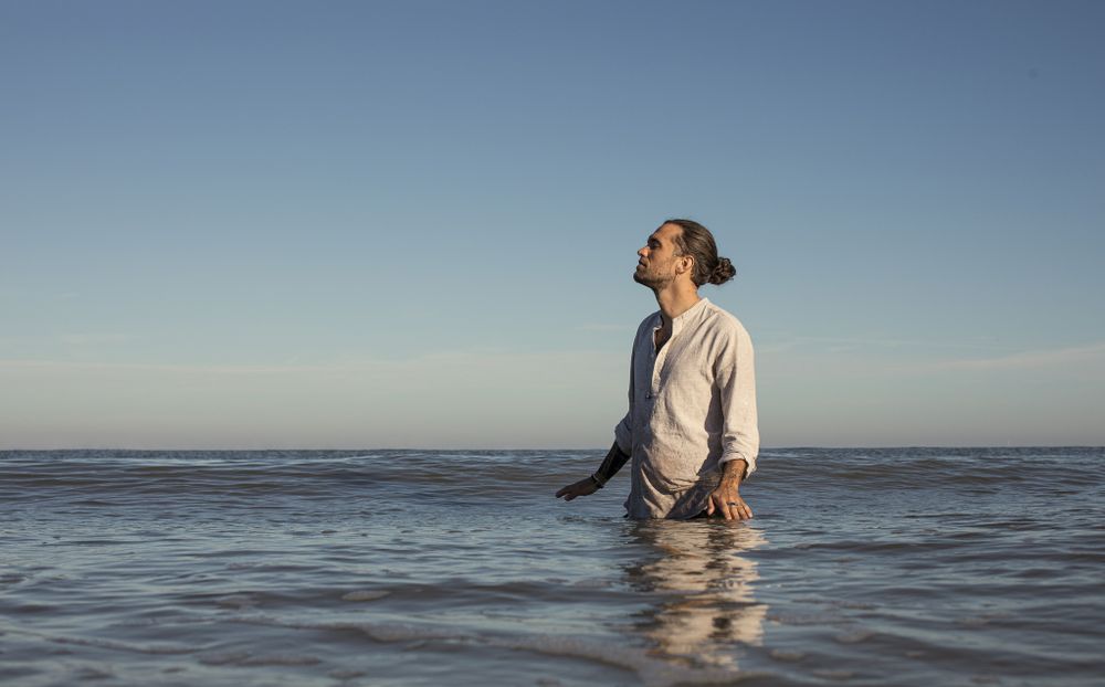 Figure wading in calm ocean waters during sunset.