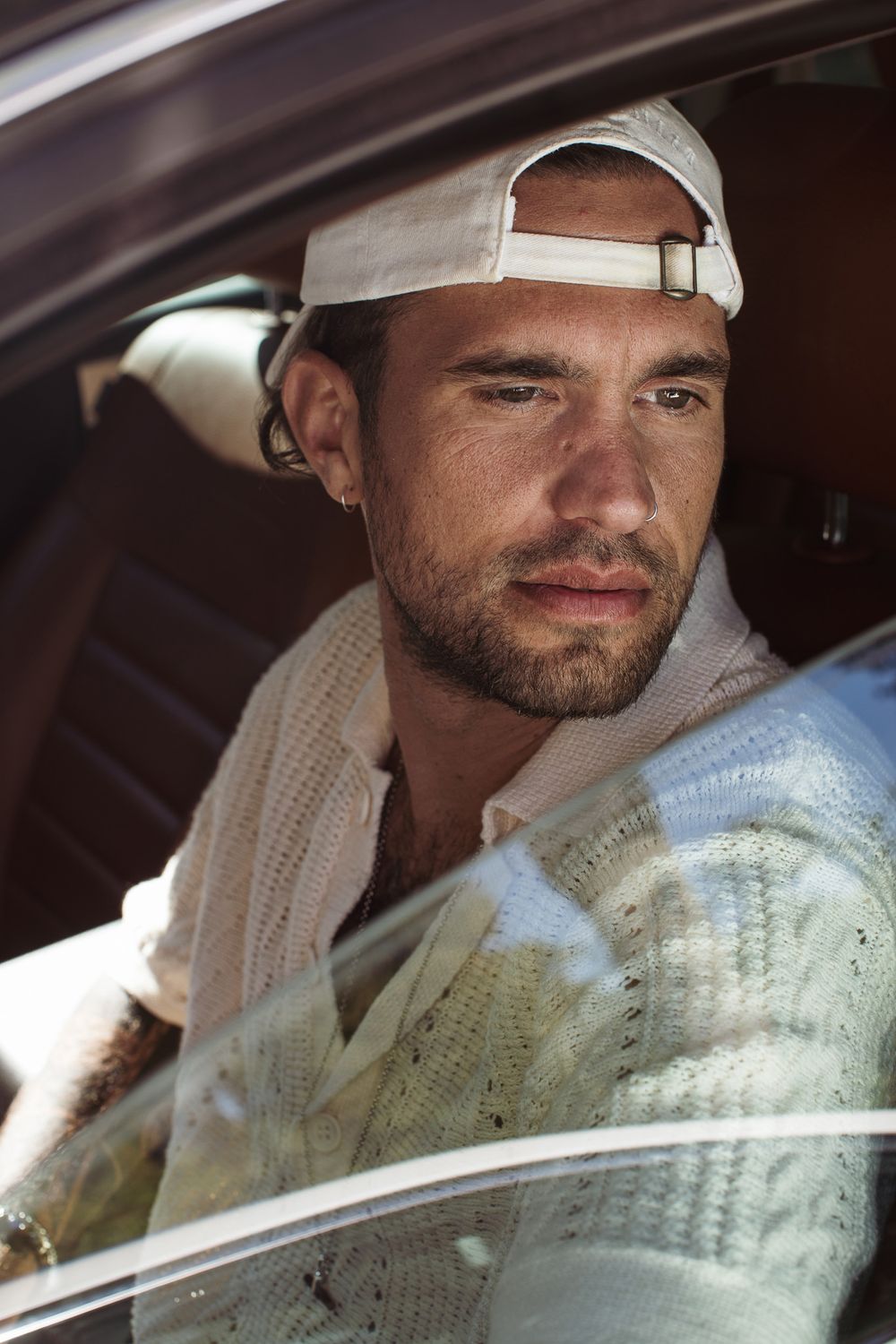 Person wearing white cap and knit sweater sitting in car with sunlight streaming through window.