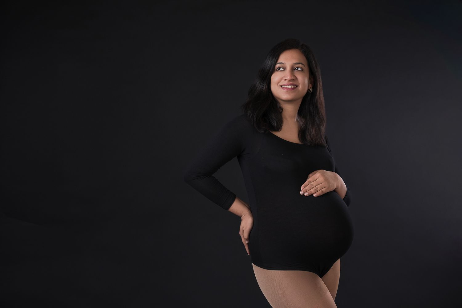 Studio maternity portrait against black background capturing joyful expression.