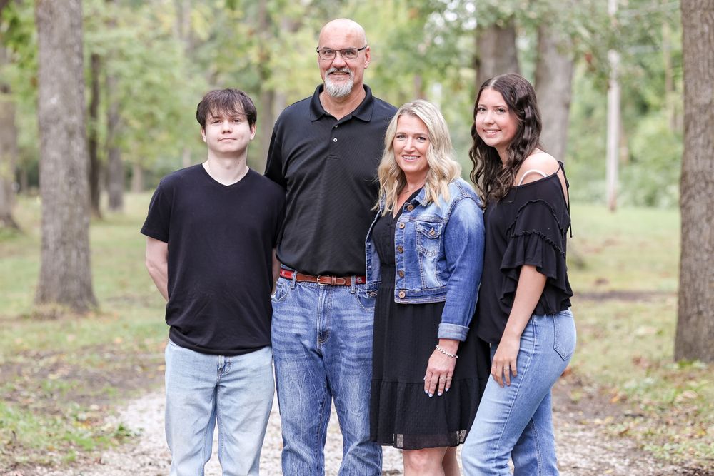Family of four stands and smiles on a trail surrounded by trees