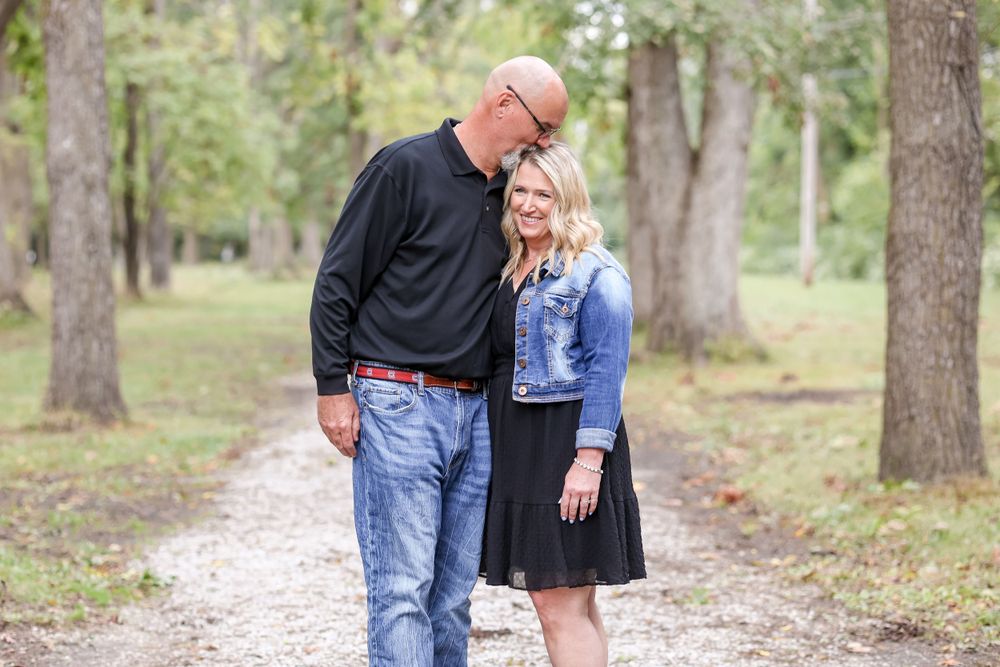 Couple stand together on a trail while man kisses woman on the head.