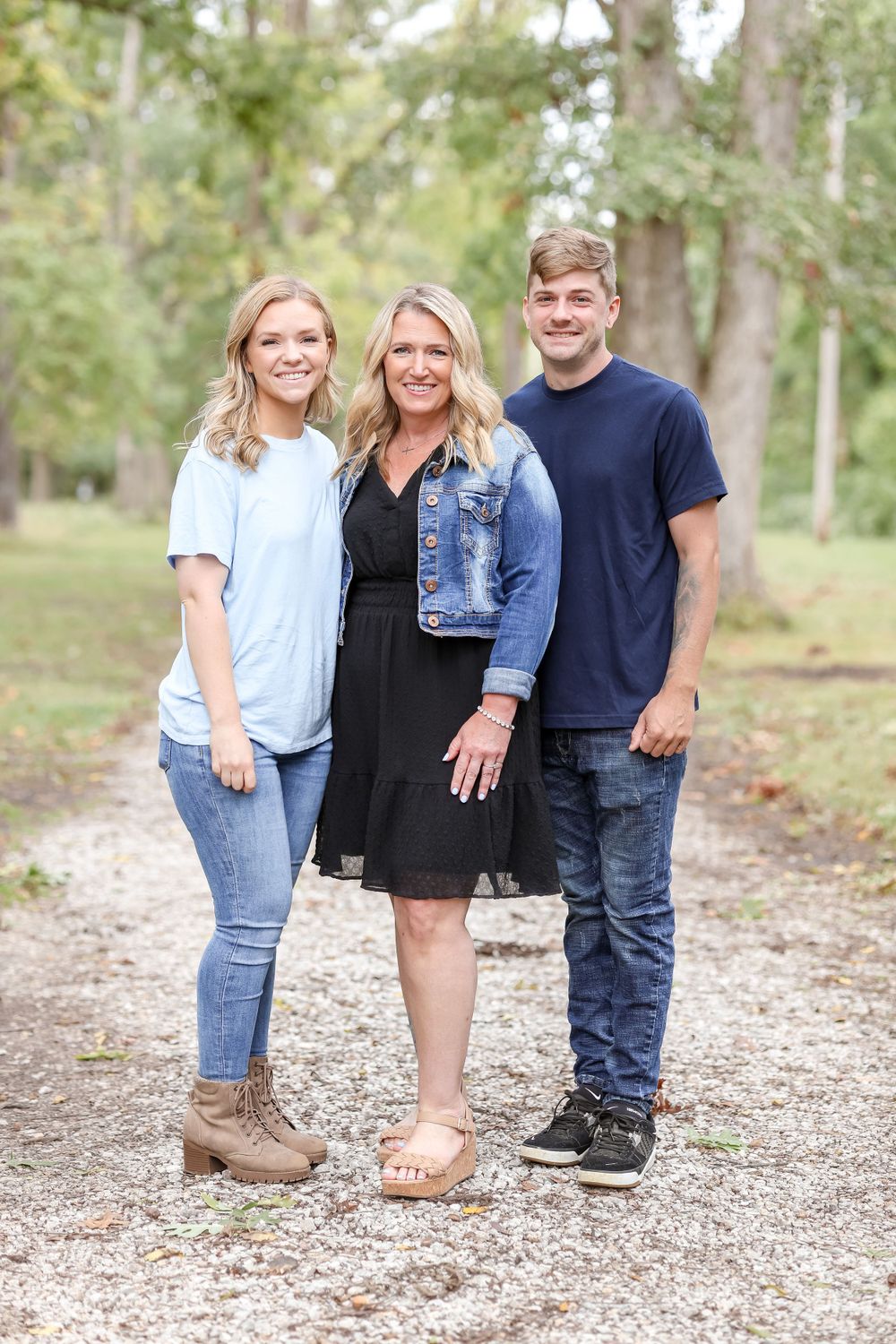 Grown siblings take a picture with their mom on a trail surrounded by trees