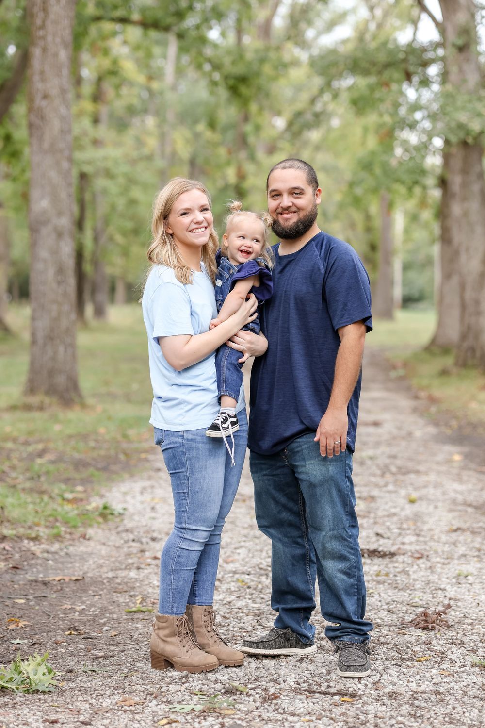 Couple and their daughter stand on trail for a picture surrounded by trees with green leaves