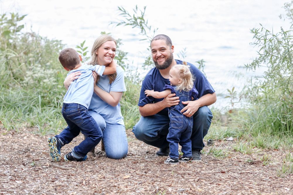Parents laugh and snuggle with their two kids on a trail lakeside