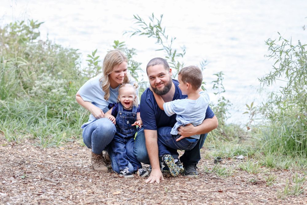 A family enjoying time together outdoors on a dirt path surrounded by green foliage on a sunny day.