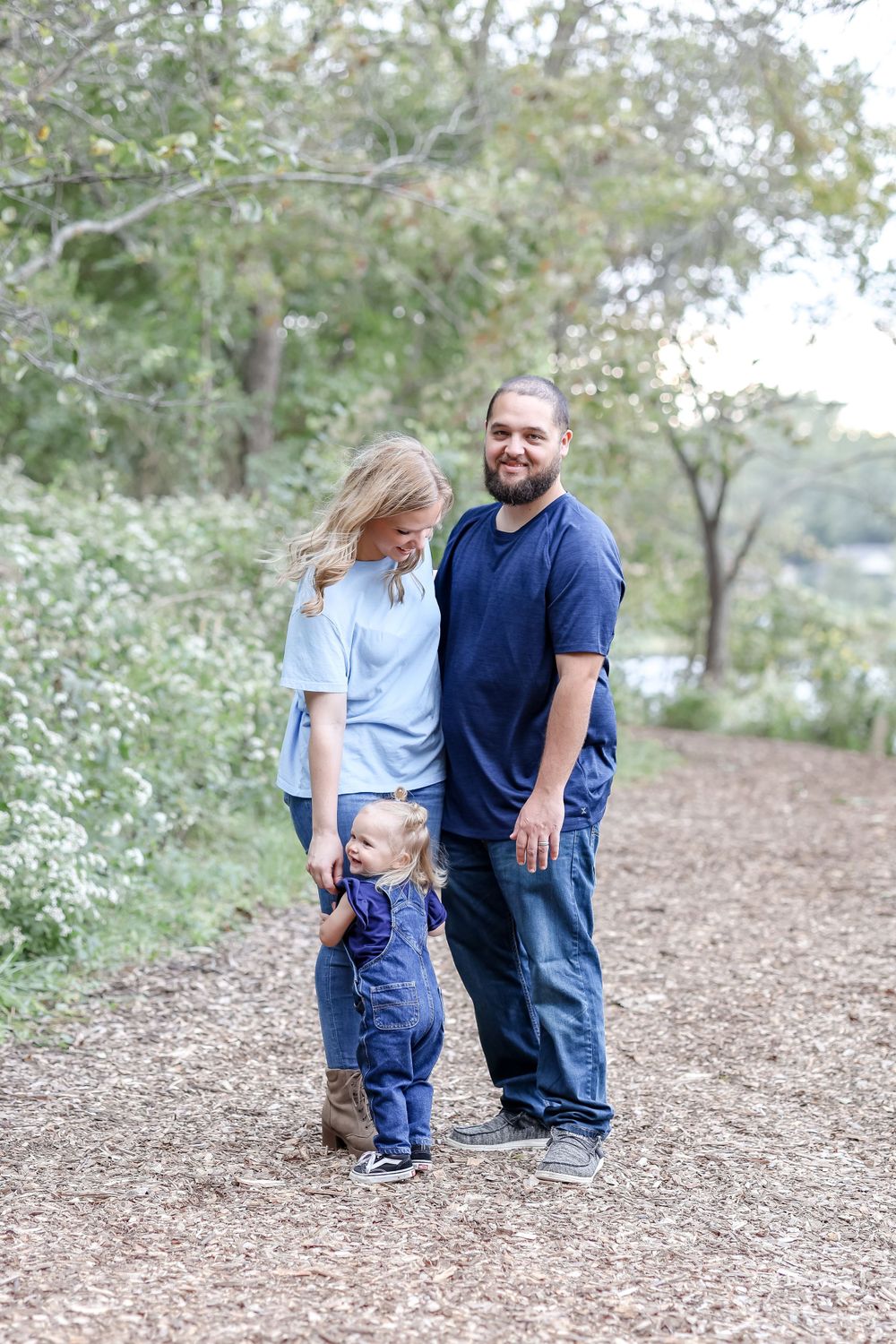 Family wearing coordinated blue outfits enjoy a casual stroll together on a natural dirt path surrounded by trees.