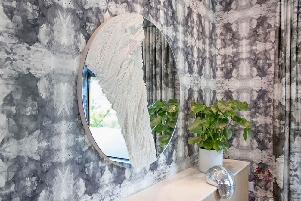 Modern bathroom with abstract wallpaper, curved mirror, and green plant accents.