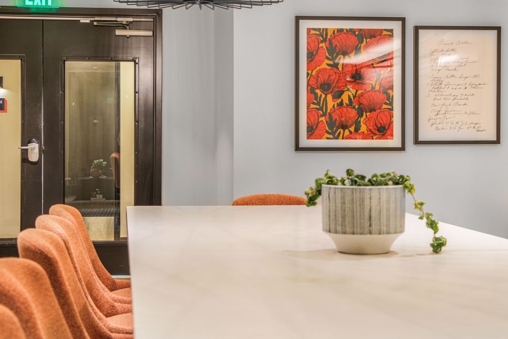 Contemporary office space with coral chairs and potted plant on white table beneath framed wall art.
