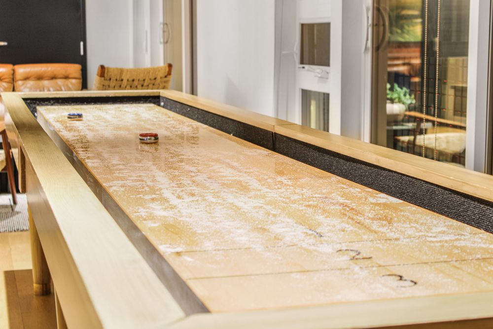 Long wooden shuffleboard table with scoring marks in modern game room setting.