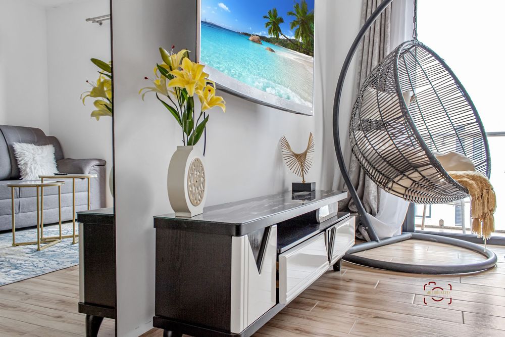 Modern coastal living room with hanging egg chair, beach artwork, and entertainment center against neutral gray walls.