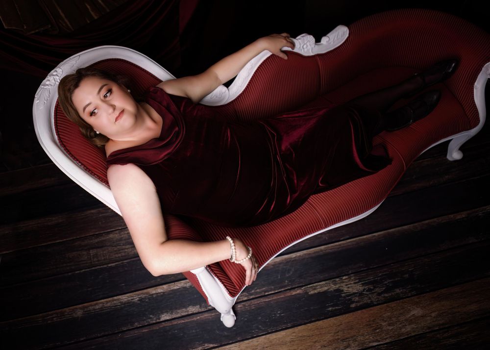 Boudoir portrait of plus size woman, woman is in crimson velvet dress and pearls.