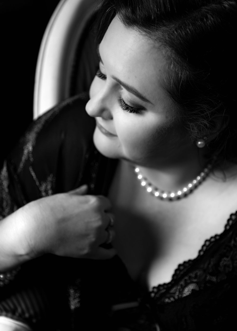 Black and white boudoir portrait of plus size woman with pearl necklace, black lace lingerie, close up.
