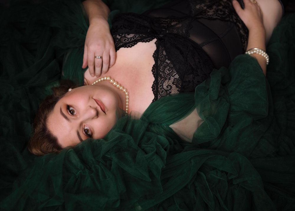 Boudoir portrait of plus size woman lying on her back on green tulle and looking up to the camera.