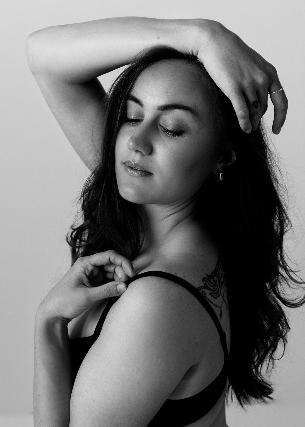 Black and white boudoir portrait close up of woman in black bra face framed by her arms.