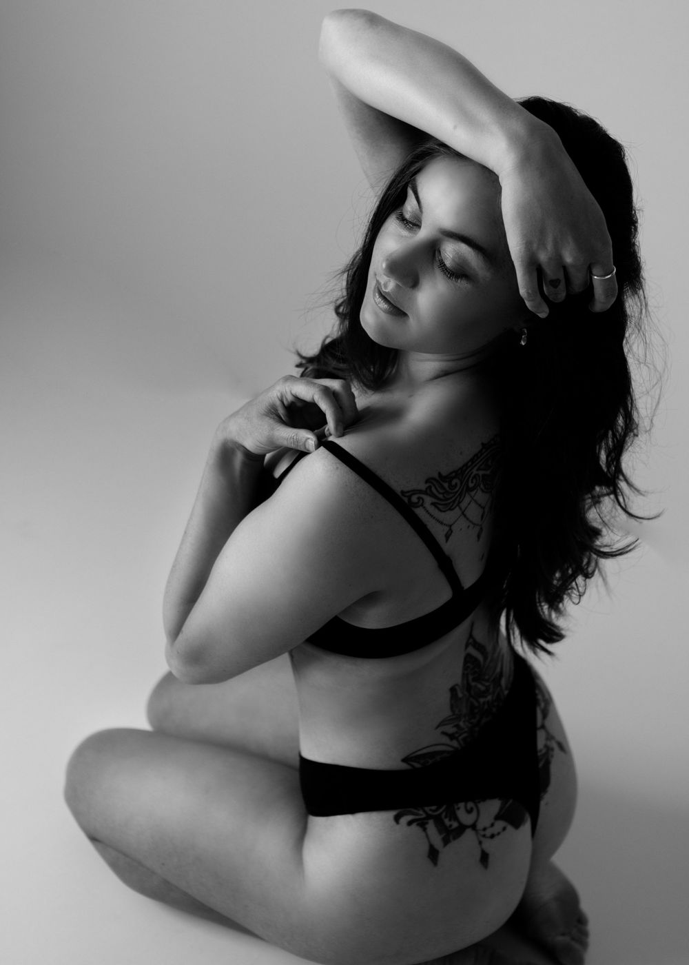 Black and white boudoir portrait of woman on her knees in studio face framed by her arms.
