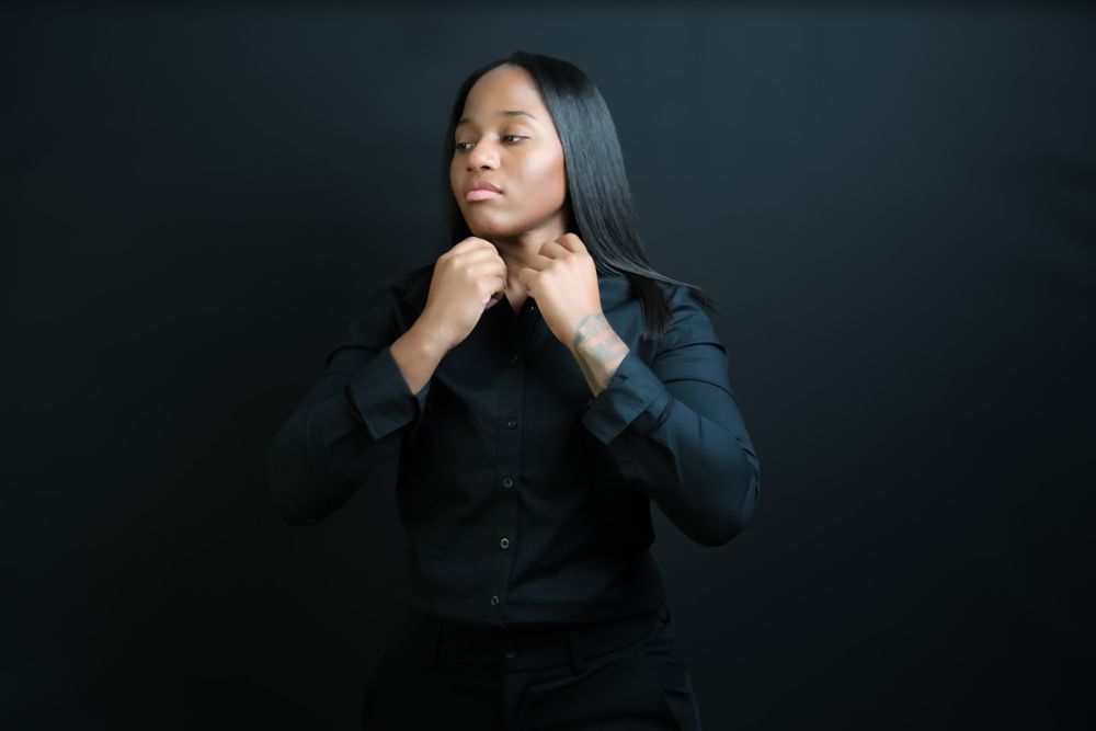 Figure poses expressively in black outfit against dark studio setting.