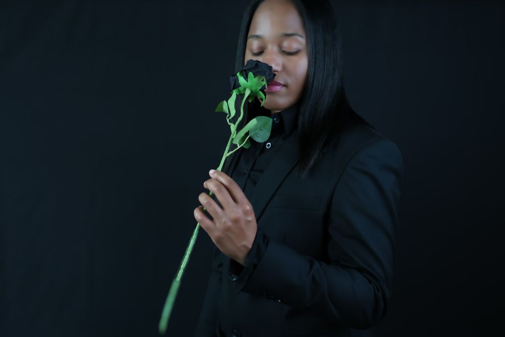 Figure in black outfit poses dramatically against dark background.