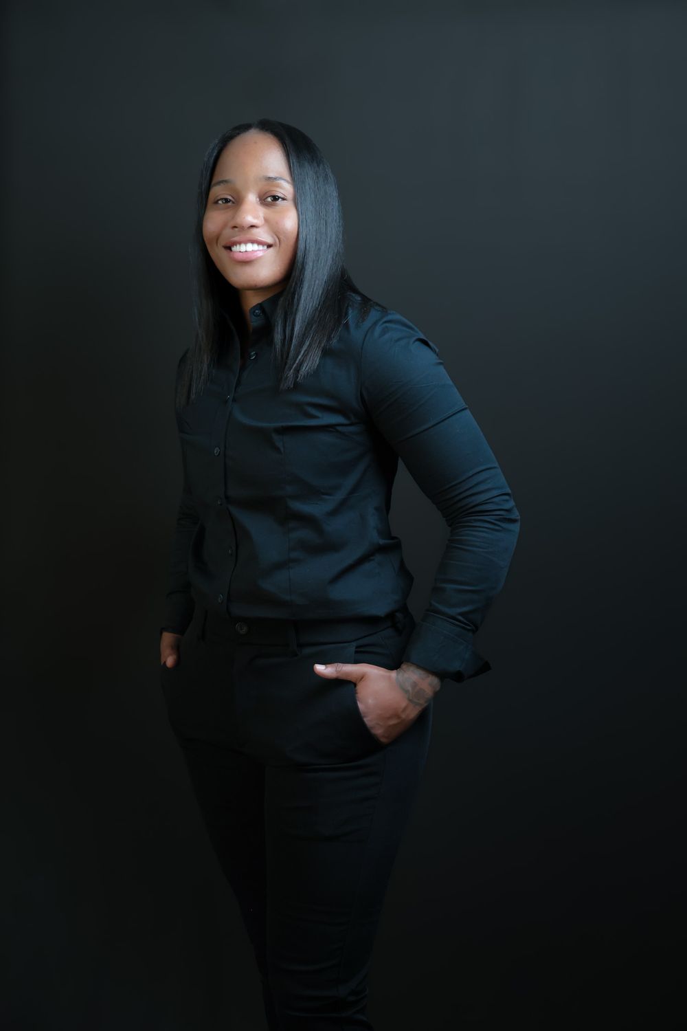 Person in all black attire strikes dynamic pose against dark studio backdrop.