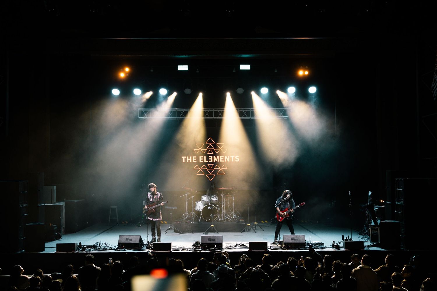 Rock band performing on stage with dramatic backlighting and spotlight effects during a concert.