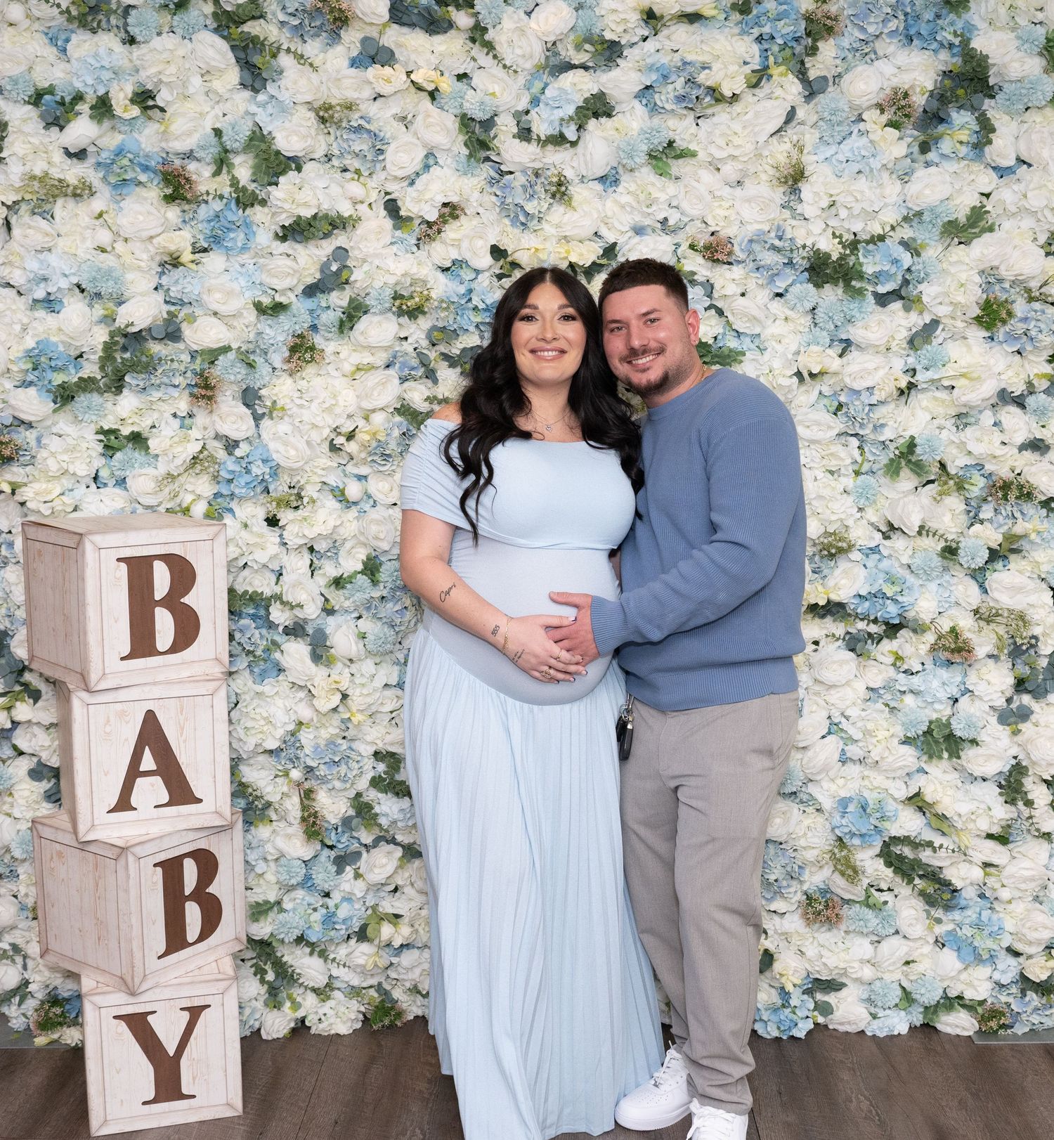 Maternity photos with wooden baby blocks and white floral wall backdrop.
