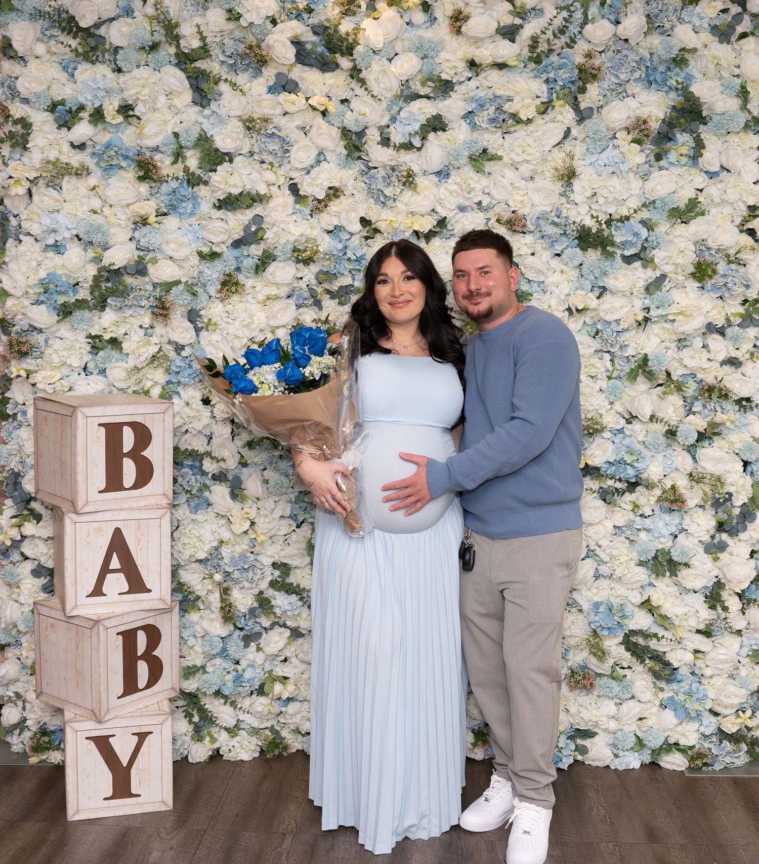 Babyshower photoshoot with decorative wooden blocks and floral backdrop.