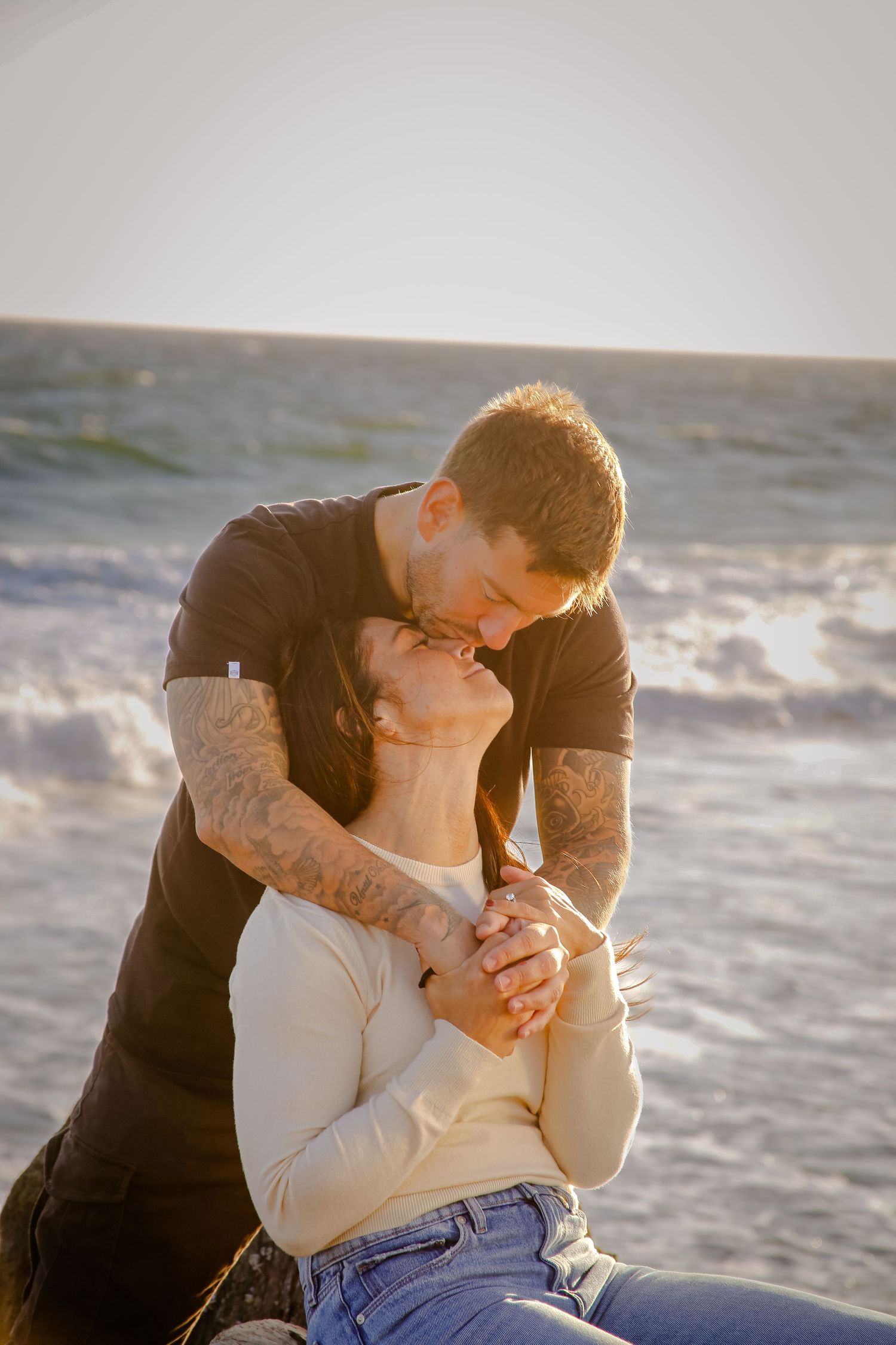 Romantic sunset beach photoshoot with couple embracing against ocean waves.