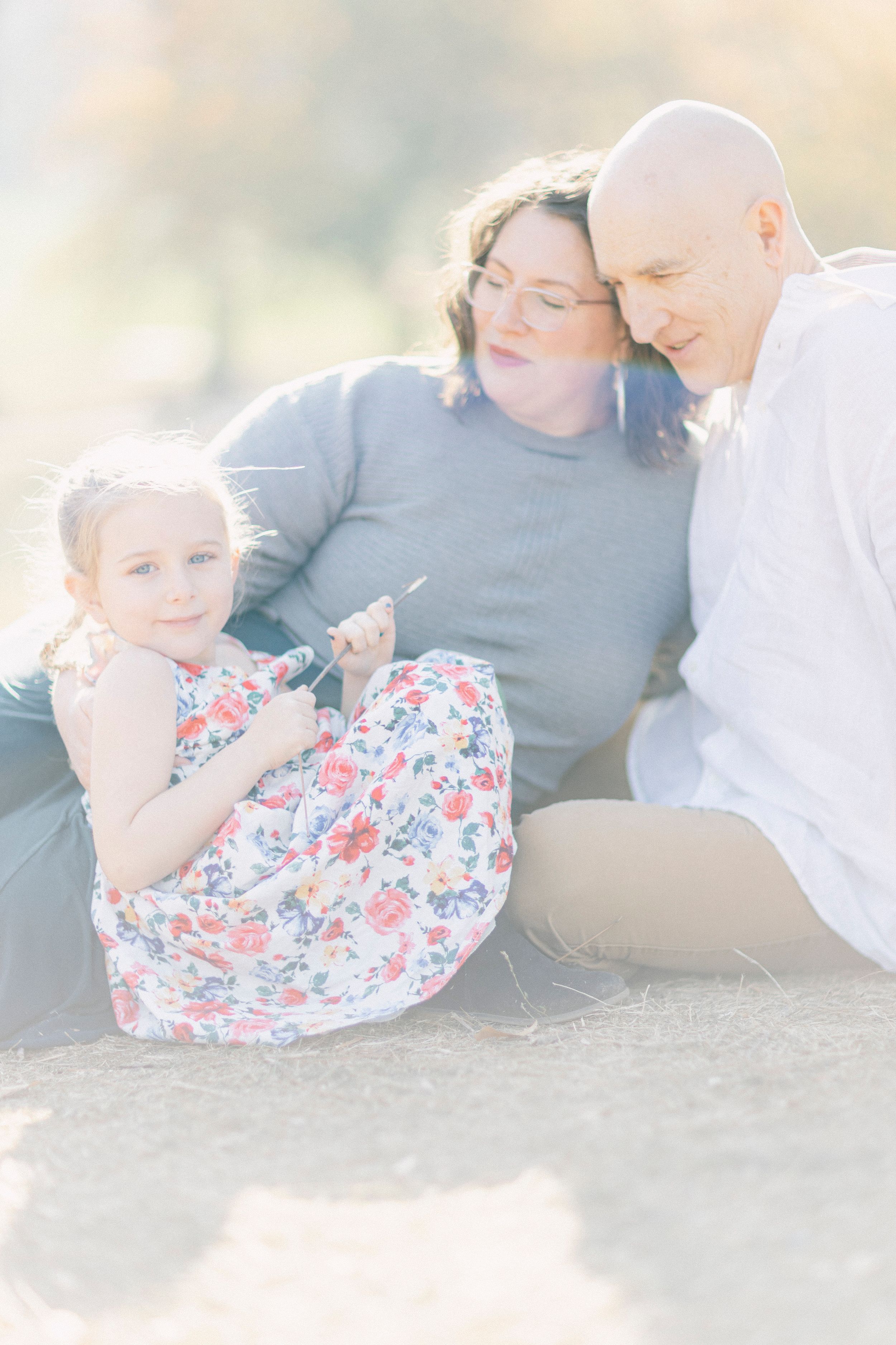 A family sits together on the ground sharing an intimate moment in soft lighting.