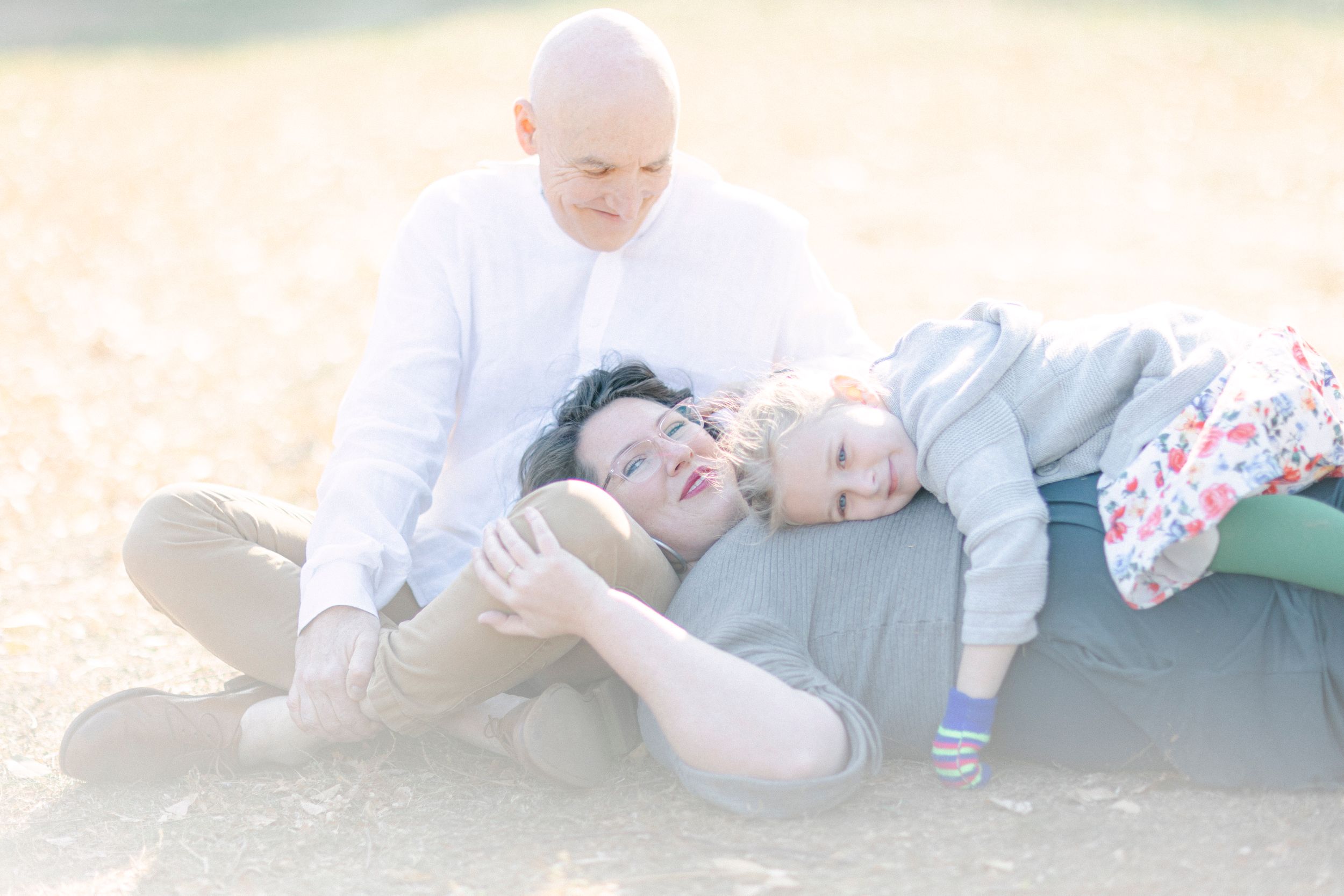 A relaxed family lying together on the ground in gentle sunlight.