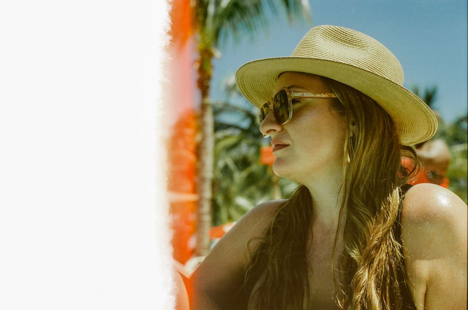 Summery beach scene with straw hat and sunglasses in warm tones with palm trees.