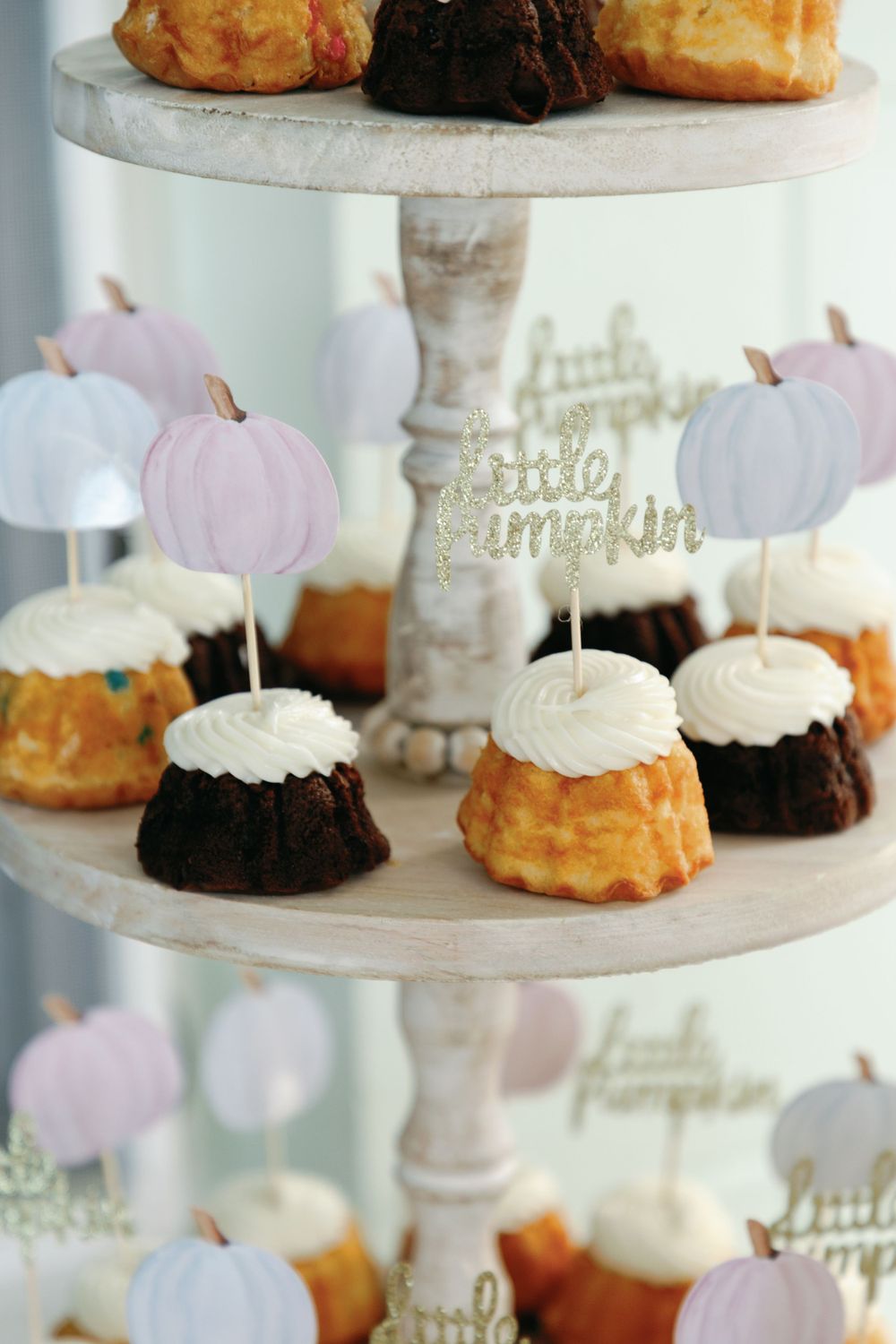 Mini bundt cakes on tiered stand with little pumpkin toppers at a gender reveal dessert table.