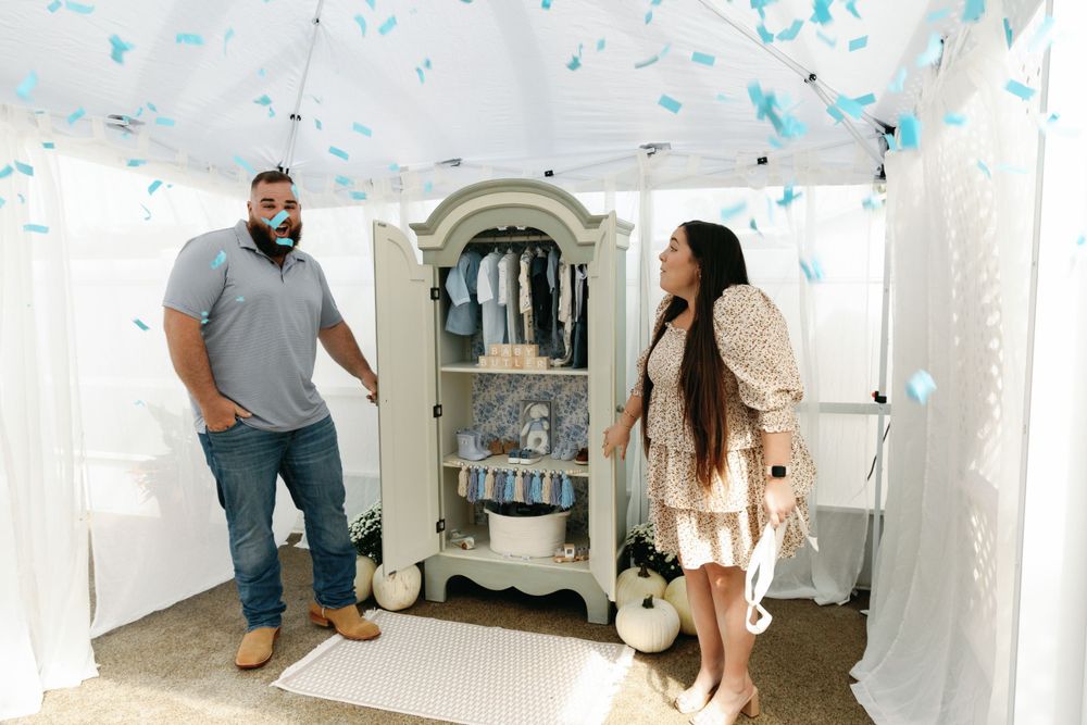 Couple reacting with surprise as blue confetti falls from armoire at gender reveal party.