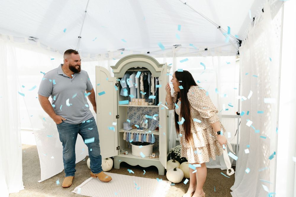 Couple laughing as blue confetti explodes from armoire revealing baby boy gender.