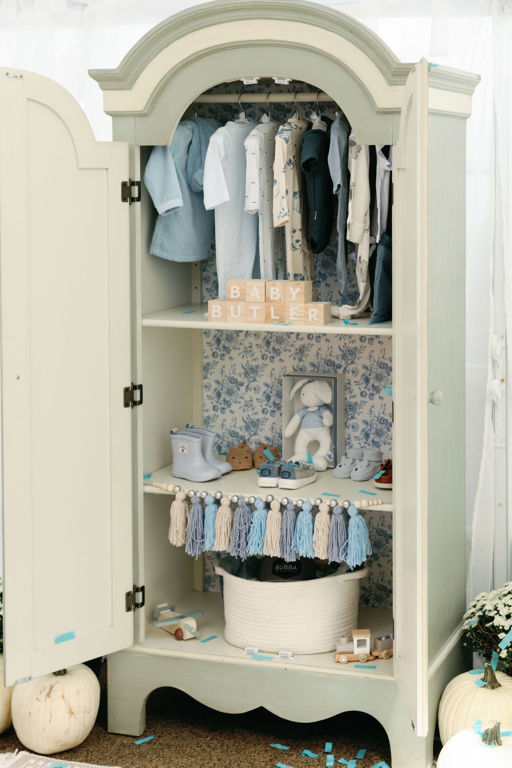 Elegant sage armoire displays Baby Butler nursery items in blue and white.