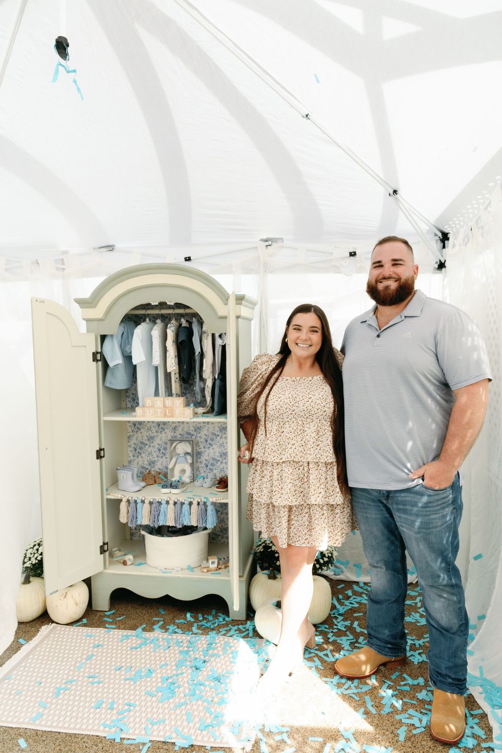 Smiling couple poses beside sage armoire after blue confetti baby gender reveal.